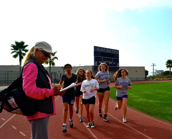 PE teacher Jane McGhee checks in students as they round the track during PE class.  McGhee treated the campus to 40 dozen doughnut holes before school on Tuesday, Feb.5 to celebrate her 40th year of teaching.