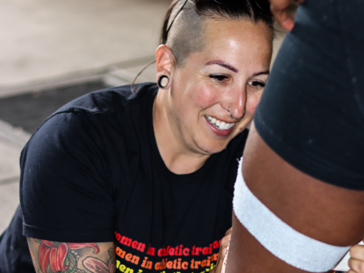 Millard wrapping an athlete's leg in medical tape as part of her daily job.
